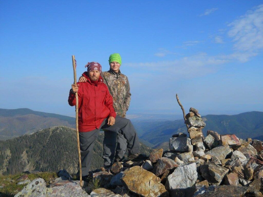 Two men on top of a mountain next to a stack of rocks.