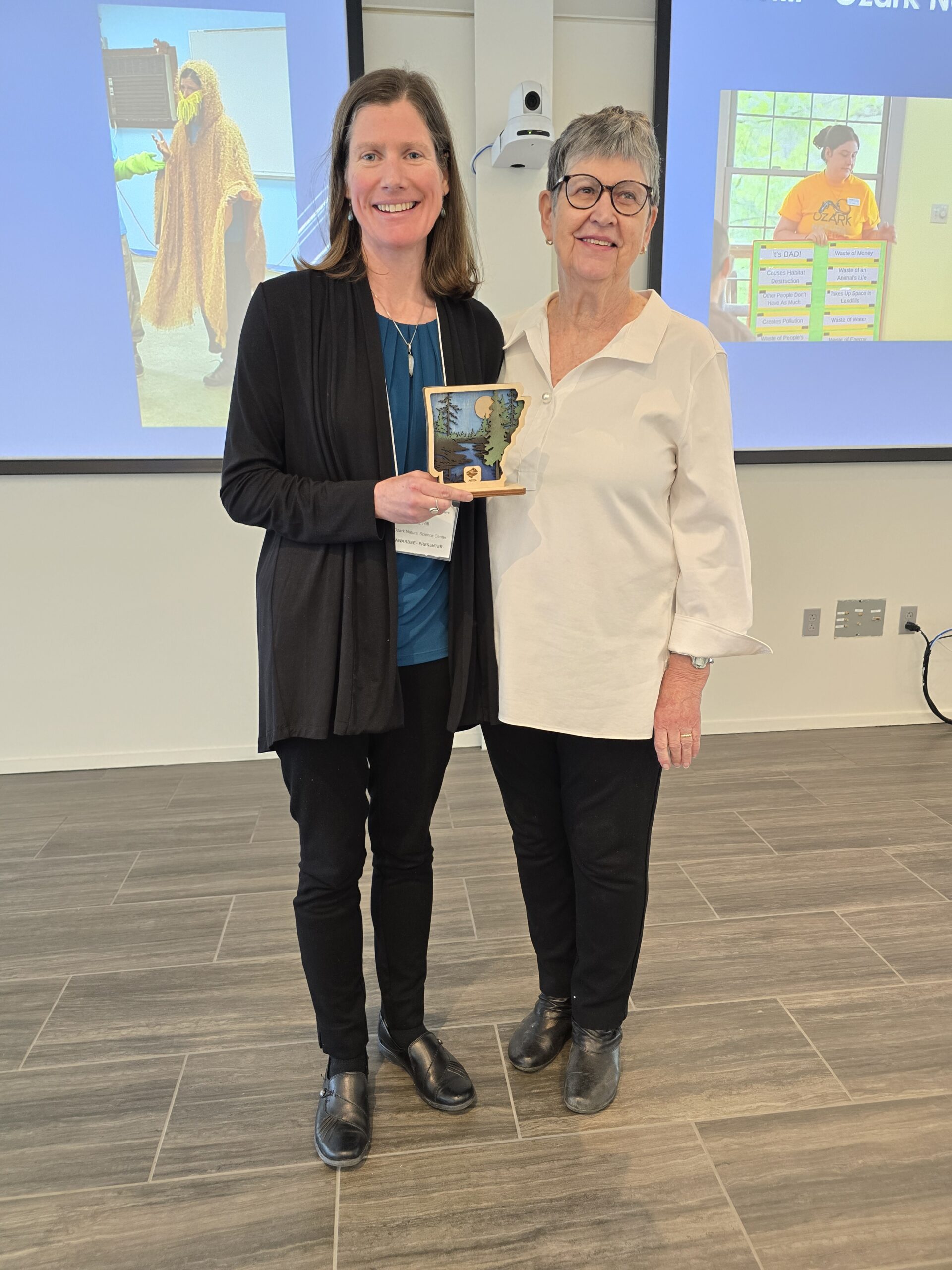 Two women standing together. One is holding a small wooden award.