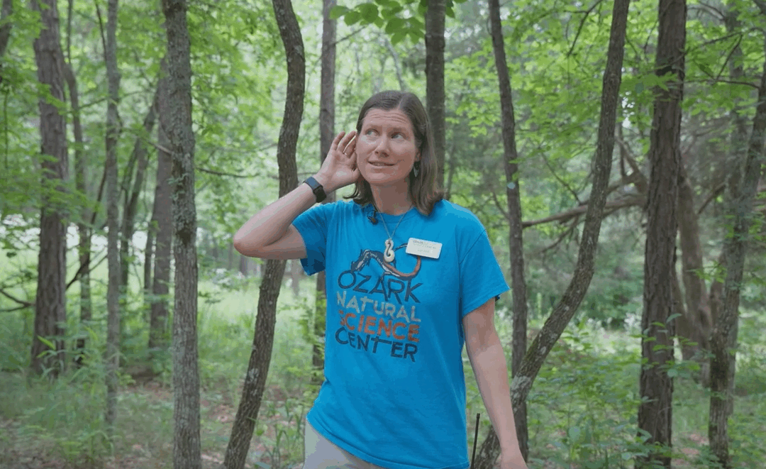 woman standing outside with her hand cupped behind her ear.