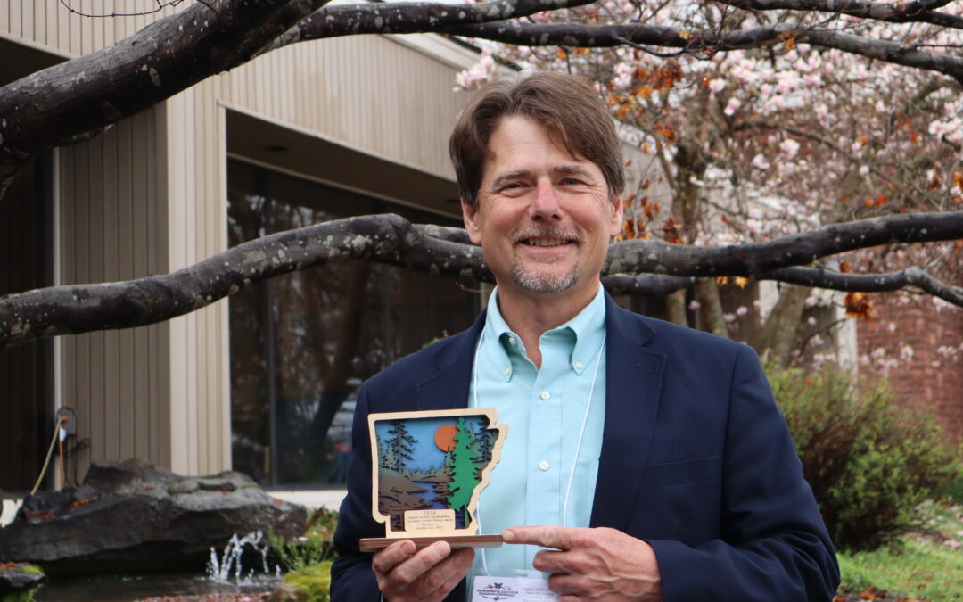 man standing outside holding a small wooden award in the shape of Arkansas